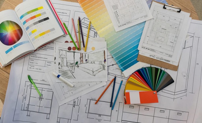 Some papers with interior design models having drawn along with color pencils and color pallette note book kept in the table.