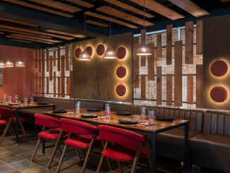 Tables and chairs are arranged with plates, spoons and glasses in a restaurant that is brightened with lantern light setting.