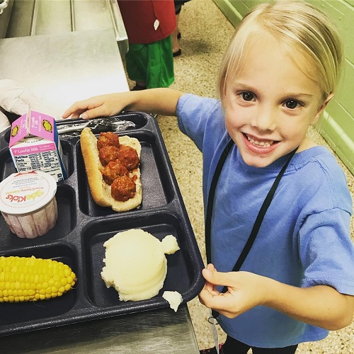 A girl is seen with her plate of lunch at the counter.